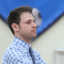 a man wearing a plaid shirt and tie is standing in front of a blue wall .