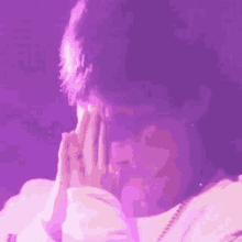 a close up of a person 's face with their hands folded in front of a purple background .