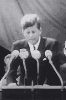 a man in a suit and tie is standing at a podium giving a speech .