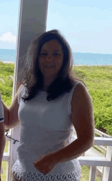 a woman in a white tank top and white shorts is standing on a balcony overlooking the ocean .