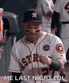 a baseball player wearing a hat and a jersey is standing in the dugout and making a funny face .