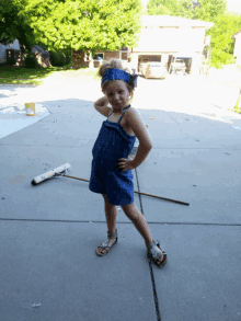 a little girl in a blue dress is standing on a concrete driveway