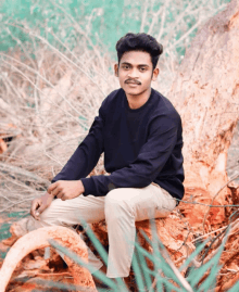 a young man in a black sweater sits on a tree trunk