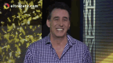 a man in a plaid shirt is smiling in front of a screen that says eltrecetv.com