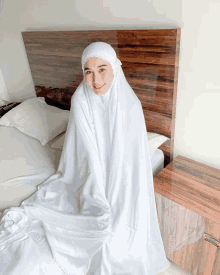 a woman wearing a white hijab sits on a bed