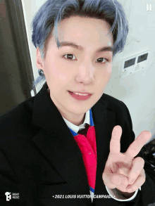 a young man with blue hair is wearing a suit and tie and making a peace sign