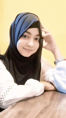 a woman wearing a hijab is sitting at a table with her hand on her forehead