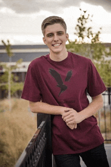 a young man wearing a maroon t-shirt is leaning against a railing .