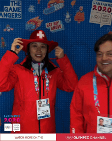 a woman wearing a red hat stands next to a man wearing a red jacket that says olympic channel on it