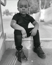 a black and white photo of a young boy sitting on a set of steps