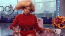 a woman in a red dress is sitting in a chair on a television show holding her hair .