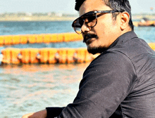 a man wearing sunglasses and a black shirt is looking at the water