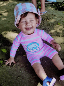 a baby wearing a pink and blue striped swimsuit and a hat