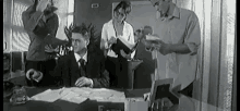 a black and white photo of a man sitting at a desk in front of a group of people .