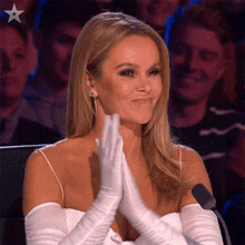 a woman wearing white gloves is clapping her hands in front of a microphone