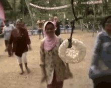 a group of people are walking down a dirt road and a woman is carrying a large white bag .