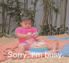 a little girl is sitting on a blanket eating a cake with the words sorry i 'm busy behind her