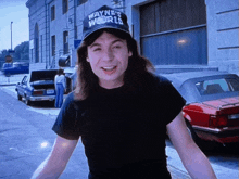 a man wearing a wayne 's world hat stands on a street