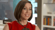 a woman in a red dress is smiling and wearing a necklace .