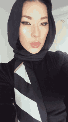 a woman wearing a black hijab and a striped scarf takes a selfie