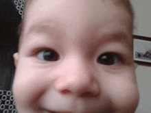 a close up of a baby 's face with a picture on the wall in the background