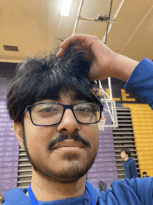 a man with glasses and a beard scratches his head in a gym