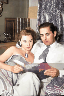 a man and woman sit on a couch reading a book