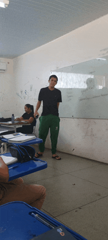 a man in a black shirt and green pants stands in front of a white board that says " a " on it