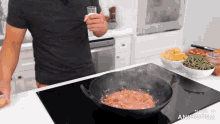 a man in a black shirt is holding a glass of milk over a pan of food on a stove top made in animatica