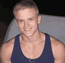 a man wearing a blue tank top and a necklace with the words it 's on top below him