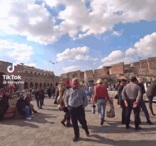 a group of people are walking down a street in front of a building with a blue sky in the background .