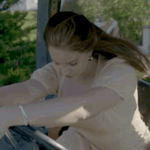 a woman is sitting in the driver 's seat of a vehicle with her hands on the steering wheel .