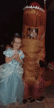 a girl in a blue dress stands next to a boy in a t-rex costume