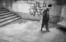 a man is walking down a sidewalk with a skateboard in front of a wall with graffiti on it