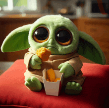 a stuffed animal with big eyes is sitting on a red pillow eating a chicken nugget