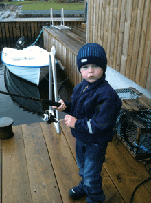 a young boy holds a fishing rod in front of a small boat