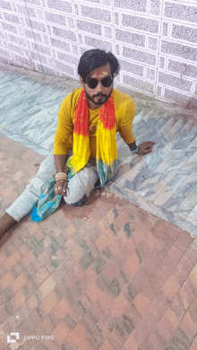 a man wearing sunglasses and a yellow shirt is sitting on a set of stairs taken by an oppo f19s