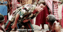 a man in a hawaiian shirt is kneeling down in front of a group of people and talking to another man .