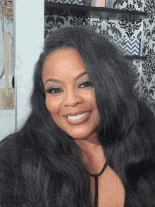 a woman with long black hair is smiling in front of a shelf with utensils on it