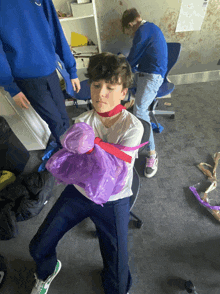 a boy with a purple bag around his neck is standing in a room