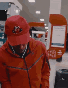 a man wearing a red jacket and a red hat stands in front of a sign that says " contactless ways to pay "