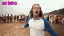 a man in a blue and white shirt is standing on a beach with a crowd behind him and the words se faire above him .