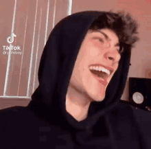 a young man wearing a black hoodie is laughing with his eyes closed .