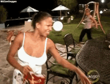 a woman in a white tank top is standing in front of a table holding a bag of chips .