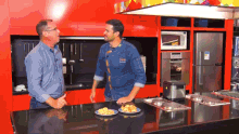 a man in a chef 's uniform is talking to another man in a kitchen with plates of food on the counter