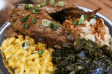 a plate of food with macaroni and cheese , collard greens , and meat on a wooden table .