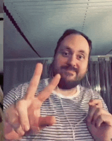 a man with a beard is wearing a striped shirt and giving a peace sign .