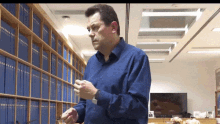 a man in a blue shirt is standing in front of a bookshelf that has a lot of blue books