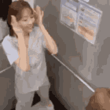 a woman is standing in an elevator with her hands on her head and a sign on the wall behind her .