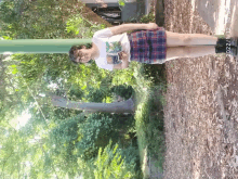 a girl wearing a plaid skirt and a t-shirt with a bear on it stands in a park